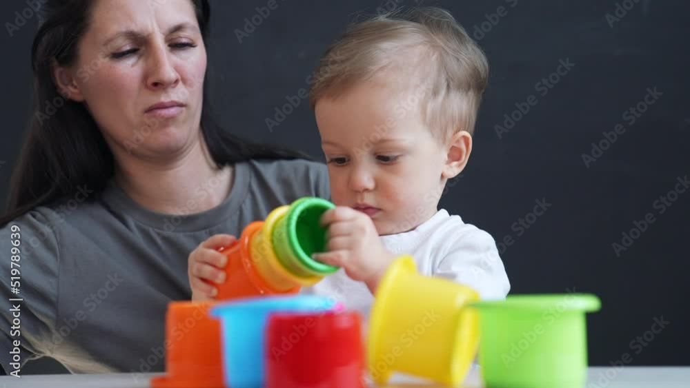 Happy cute family at home. Child collects colored cubes. Mom with her baby son play with toys at home. Happy family concept. Parent helps son in learning. Preschool family education. Mom and baby play Happy cute family at home. Child collects colored cubes. Mom with her baby son play with toys at home. Happy family concept. Parent helps son in learning. Preschool family education. Mom and baby play
