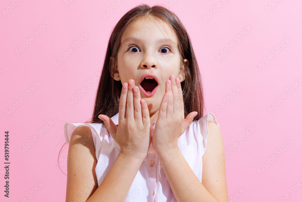 Surprised little charming girl, kid looking at camera with open mouth isolated on pink background. Concept of children emotions, fashion, beauty Surprised little charming girl, kid looking at camera with open mouth isolated on pink background. Concept of children emotions, fashion, beauty