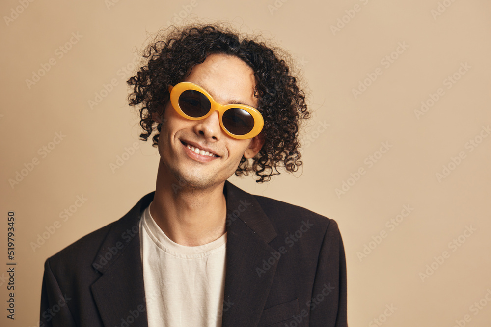 Closeup portrait of awesome tanned curly man in classic brown jacket trendy sunglasses posing isolated on beige pastel background. Fashion New Collection offer. Retro style concept. Free place for ad Closeup portrait of awesome tanned curly man in classic brown jacket trendy sunglasses posing isolated on beige pastel background. Fashion New Collection offer. Retro style concept. Free place for ad