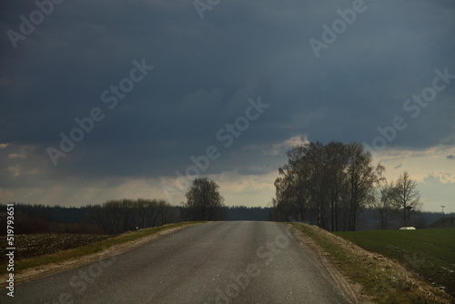 Dark stormy clouds over asphalted countryside road at spring evening