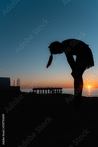 Silhouette of a tired girl at sunset. The girl is leaning over and holding on to her knees
