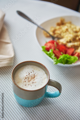 Cappuccino coffee in cup and plate with scrambled eggs and tomatoes. Breakfast on the table