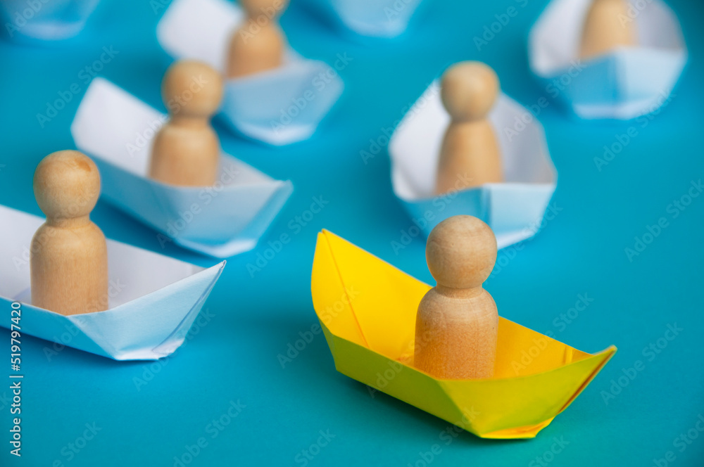 Leadership Concept - Wooden figure on yellow paper ship origami leading the rest of the figure on white paper ship. Leadership Concept - Wooden figure on yellow paper ship origami leading the rest of the figure on white paper ship.