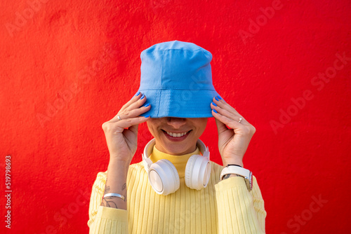 Smiling woman with headphones covering face with blue bucket hat