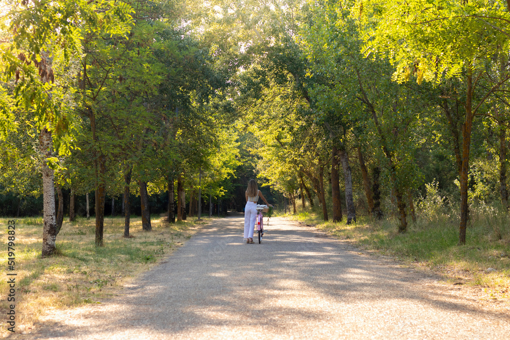 Far view of young woman alone carrying a bicycle on her side sorrounded by natural enviroment Far view of young woman alone carrying a bicycle on her side sorrounded by natural enviroment