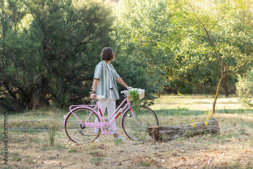 Side view of unrecognizable back looking young long haired man holding a pink vintage cute bike in the park