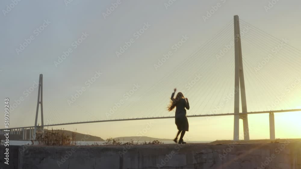 Aerial panoramic view of a woman in coat with long hair dancing in artistic manner. The Russian bridge across Eastern Bosphorus strait, Vladivostok Aerial panoramic view of a woman in coat with long hair dancing in artistic manner. The Russian bridge across Eastern Bosphorus strait, Vladivostok