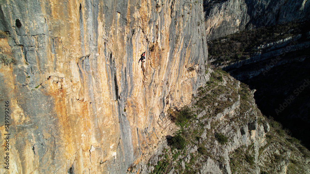 AERIAL: Sporty young woman climbing in the middle of the sunlit limestone wall AERIAL: Sporty young woman climbing in the middle of the sunlit limestone wall