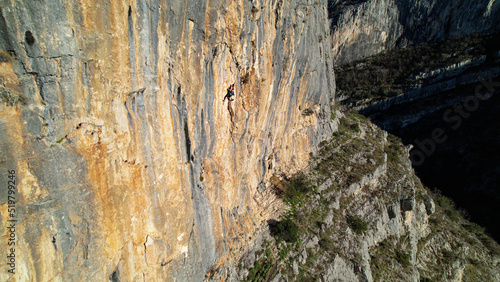 AERIAL: Sporty young woman climbing in the middle of the sunlit limestone wall