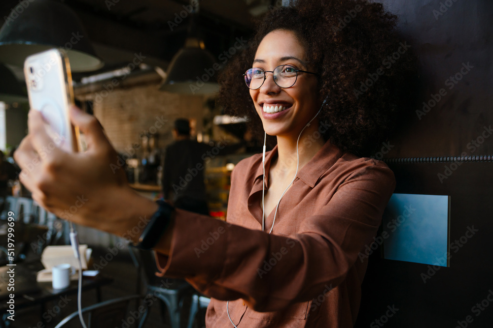 African woman smiling while using cellphone and earphones in cafe