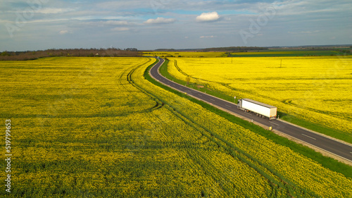 AERIAL: Cargo truck on a delivery mission moving across flowering farm landscape © helivideo