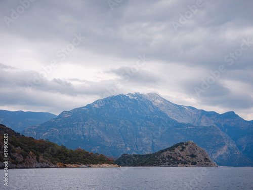 travel to Lagoon in Oludeniz, Fethiye, Turkey. beach near Darbogaz. with view to Mount Babadag, Winter landscape with mountains, green forest, azure water, beach and cloudy sky