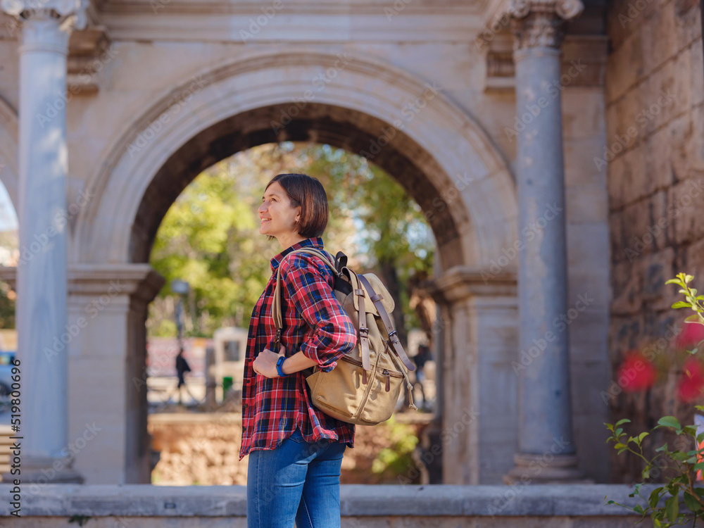 travel to Turkey. Happy asian female tourist traveller with backpack walks in old city. Woman against backdrop of Hadrian's gate - popular attraction in old city of Antalya