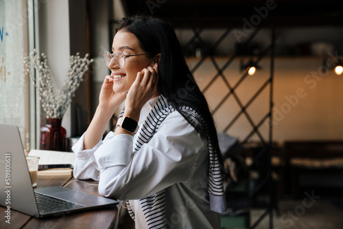 White woman in earphones working with laptop while sitting at cafe