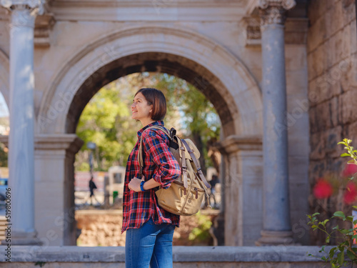 travel to Turkey. Happy asian female tourist traveller with backpack walks in old city. Woman against backdrop of Hadrian's gate - popular attraction in old city of Antalya