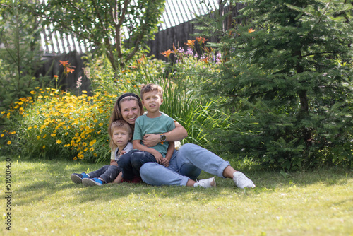 A young woman is lying on the grass with her two sons and they are laughing