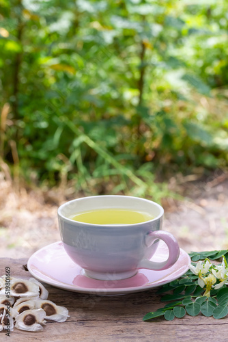 Moringa Tea in cup and fresh green leaf, flower and seeds on wooden with blur background. Moringa oleifera tropical herb healthy lifestyle concept.