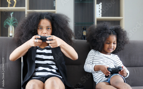 Black sister and cute African American woman having fun holding game joystick sitting on the sofa