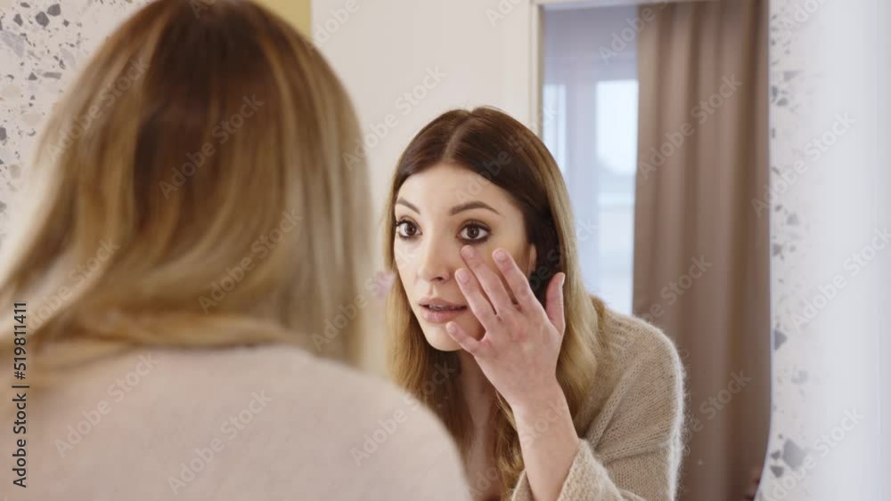 A young woman worried about the condition of her skin. He is looking at the new wrinkles on his face in the bathroom mirror. A young woman worried about the condition of her skin. He is looking at the new wrinkles on his face in the bathroom mirror.