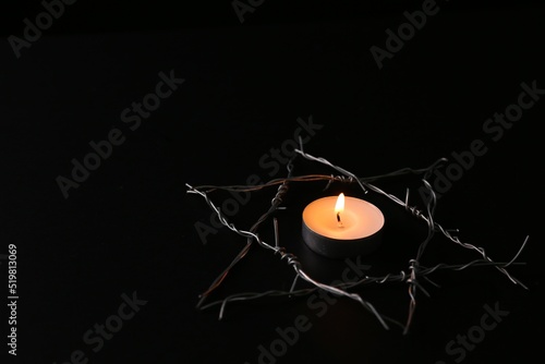 Burning candle and star of David made with barbed wire on black background. Holocaust memory day photo