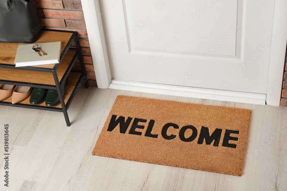 Door mat with word Welcome on wooden floor in hall - obrazy, fototapety, plakaty 