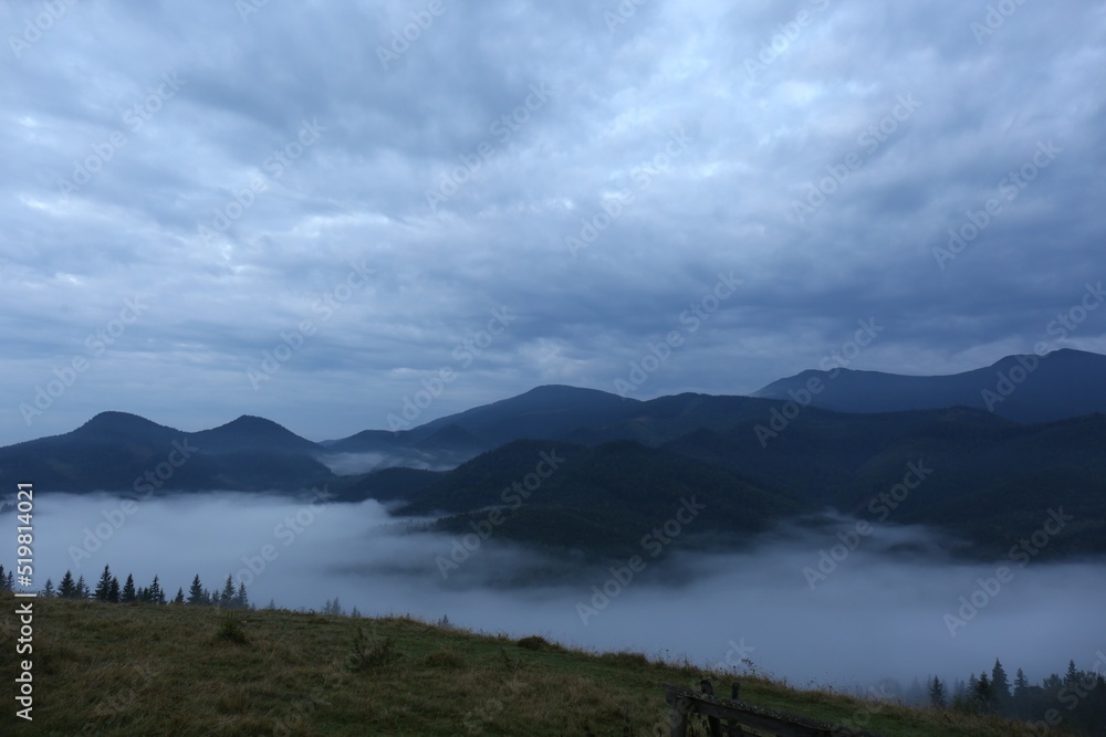 Picturesque view of mountains covered with fog under cloudy sky