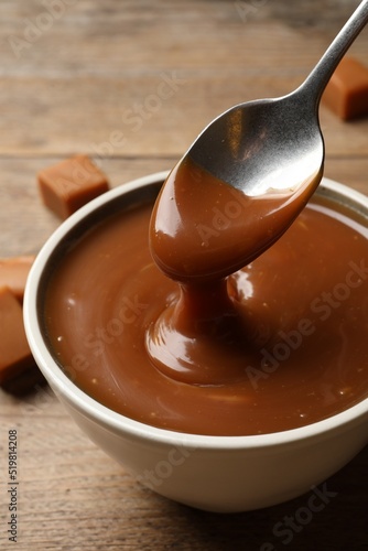 Taking yummy salted caramel with spoon from bowl at wooden table  closeup