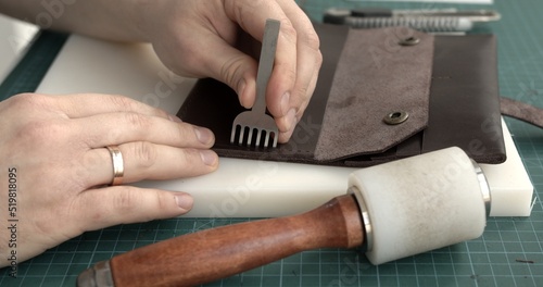 Punching holes in the leather with a hole punch with a hammer. Craftsman making holes in leather with puncher tool. Sewing wallet.