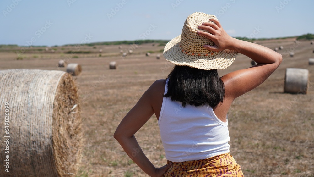 Attractive brunette woman wearing pareo and hat feeling free and happy in a cereal field with wheels of straw all over the field, she feels powerful and happy