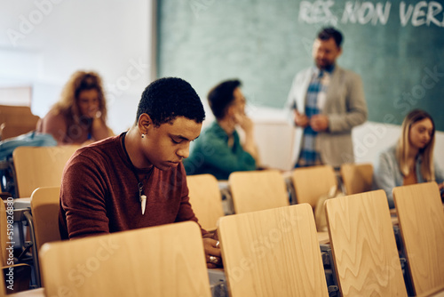 Black college student writing an exam in lecture hall.