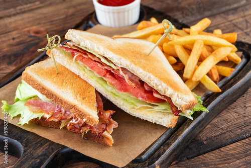 Club sandwich on a wooden board. Next to French fries and a cup of ketchup sauce