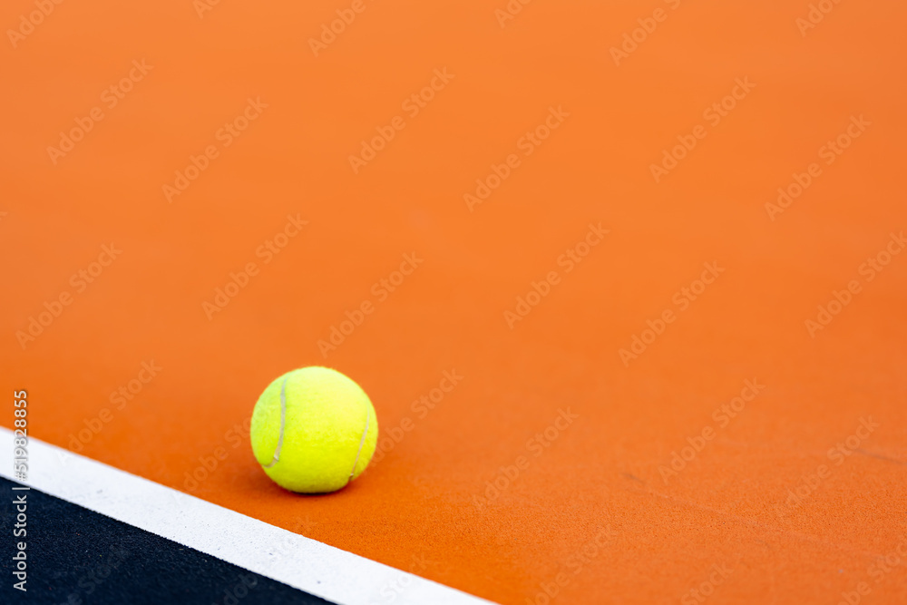 Yellow tennis ball at orange tennis court with white baseline and black out of bounds	