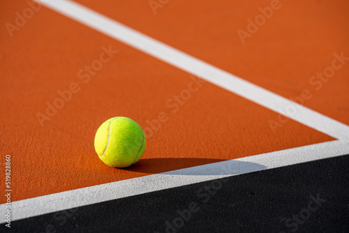 Yellow tennis ball at new outdoor orange tennis court with white baseline and black out of bounds 