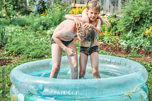 Фотография Brothers wrestle in children inflatable pool in cottage yard against lush greenery and flowers