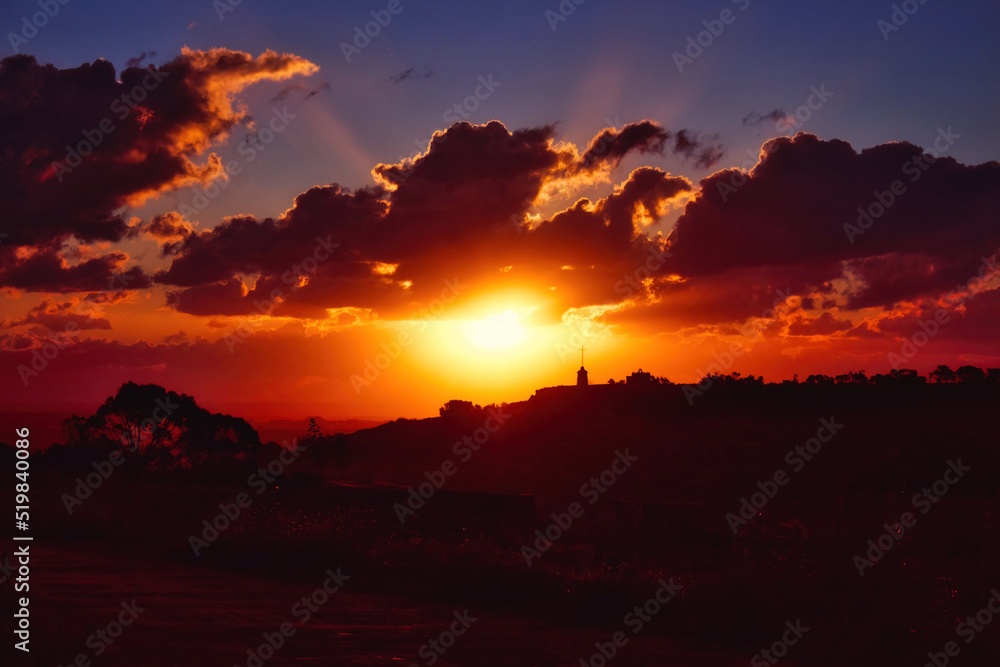 Dramatic sunset scene over hills in the countryside with deep shades of orange, red and blue
