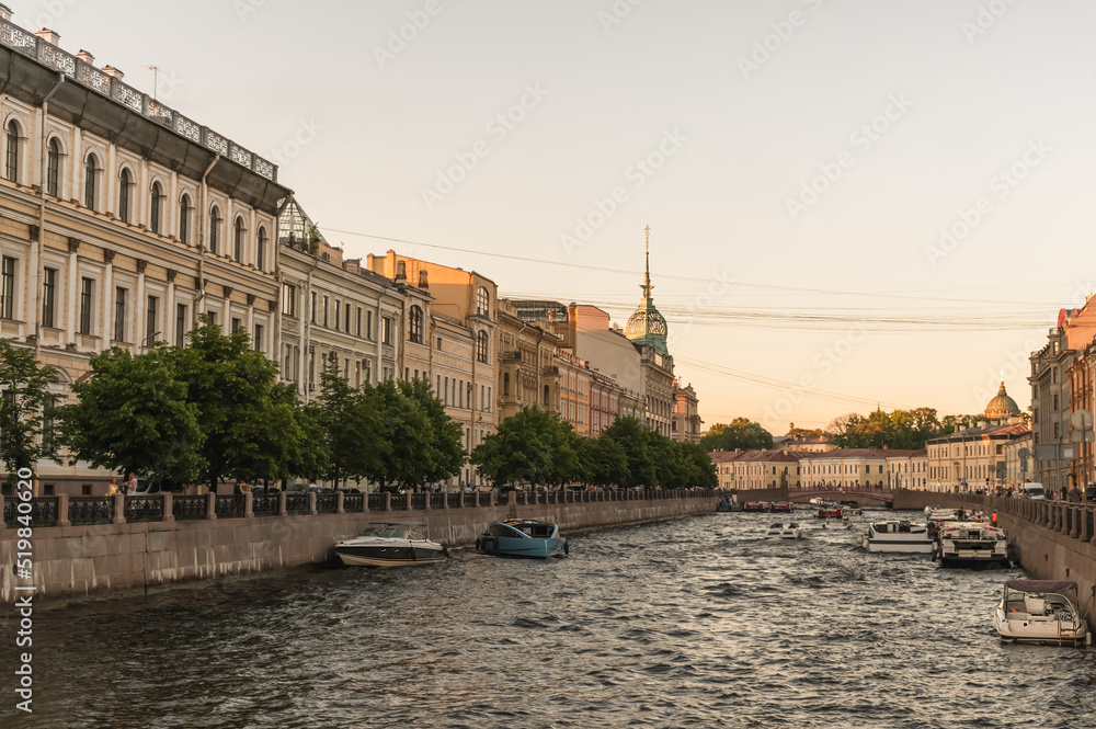 View of the Moika River and a string of pleasure boats with tourists. City landscape of St. Petersburg.Golden hour. White Nights.