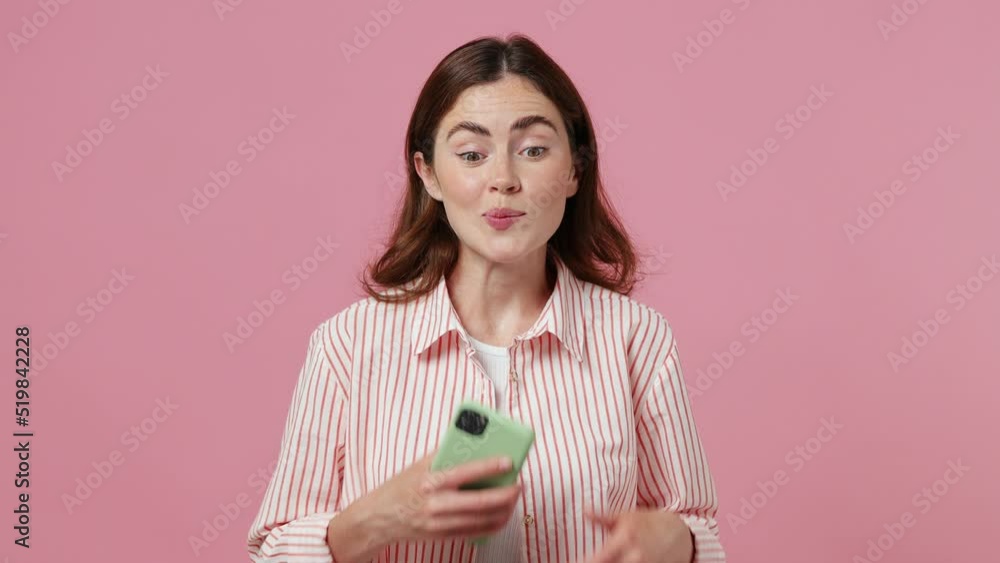 Young dreamful pensive minded bored woman 20s she wear shirt t-shirt hold using mobile cell phone typing browsing chat send sms isolated on plain pastel light pink background People lifestyle concept Young dreamful pensive minded bored woman 20s she wear shirt t-shirt hold using mobile cell phone typing browsing chat send sms isolated on plain pastel light pink background People lifestyle concept