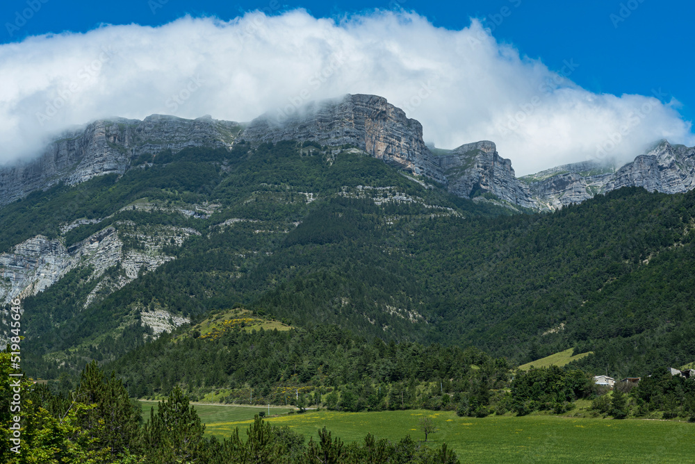 Vercors mountains under clouds in Die region with green land and farms underneath