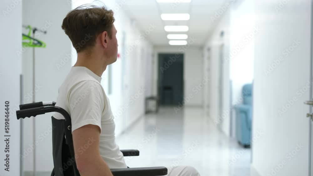 Side view devastated Caucasian ill man in wheelchair in hospital corridor looking away waiting and looking at camera. Portrait of sad depressed patient in medical clinic alone. Disability frustration Side view devastated Caucasian ill man in wheelchair in hospital corridor looking away waiting and looking at camera. Portrait of sad depressed patient in medical clinic alone. Disability frustration