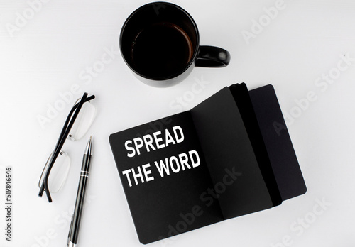 SPREAD THE WORD written text in small black notebook with coffee , pen and glasess on white background. Black-white style