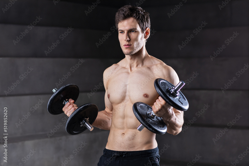 Attractive muscular man is posing with dumbbell. Fitness instructor.