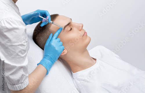 Men s cosmetology. Beautician makes a man a rejuvenation injection procedure of a handsome young man in a beauty salon.