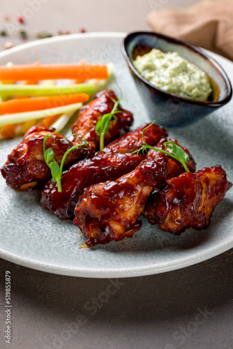 chicken wings in barbecue sauce on plate with blue cheese sauce macro close up on brown stone table vertical