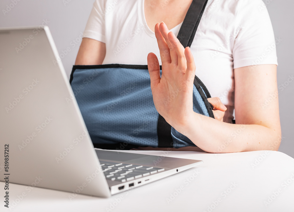 Woman with arm in sling using laptop for video call. Female waving hand to greet smb while talking online. Work, study from home due to injury. High quality photo Woman with arm in sling using laptop for video call. Female waving hand to greet smb while talking online. Work, study from home due to injury. High quality photo