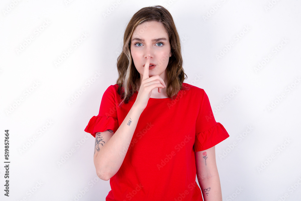 young caucasian woman wearing red T-shirt over white background makes silence gesture, keeps finger over lips. Silence and secret concept. young caucasian woman wearing red T-shirt over white background makes silence gesture, keeps finger over lips. Silence and secret concept.
