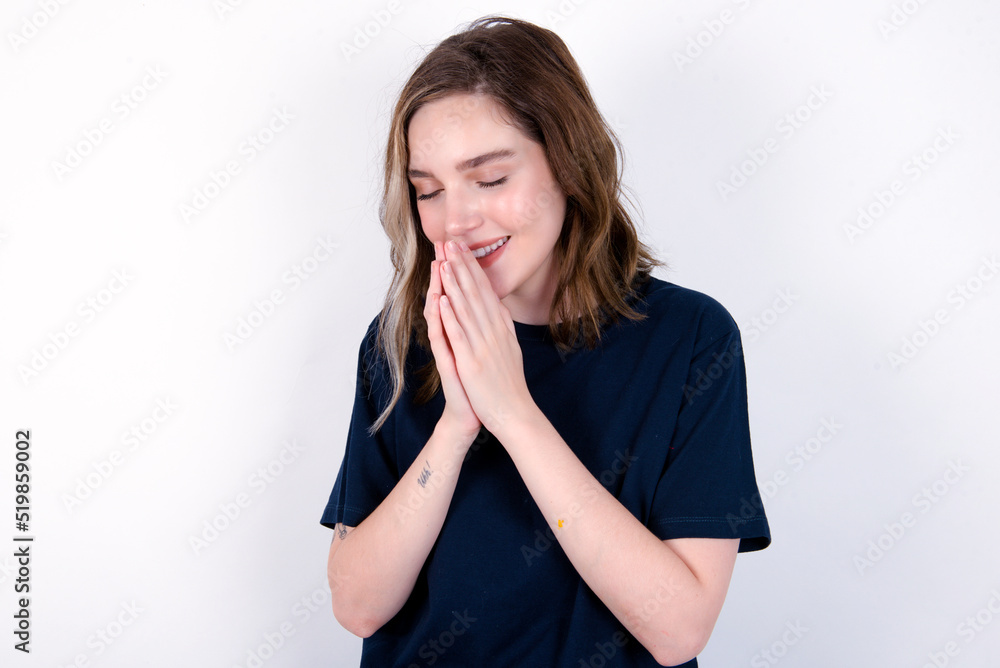 Overjoyed young caucasian woman wearing black T-shirt over white background laughs joyfully and keeps palms pressed together hears something funny Overjoyed young caucasian woman wearing black T-shirt over white background laughs joyfully and keeps palms pressed together hears something funny