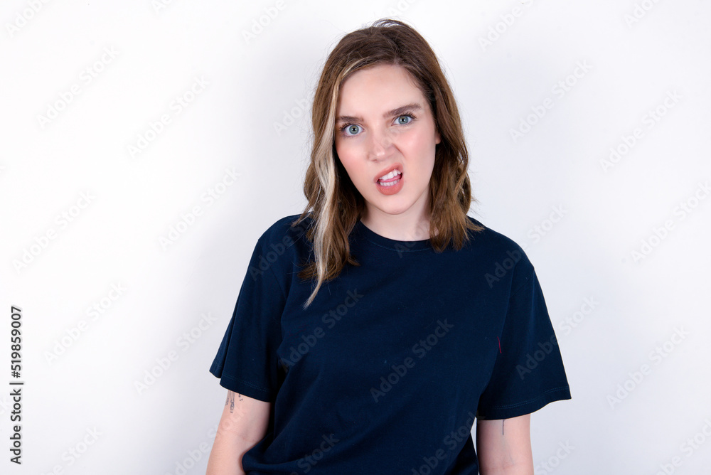 Portrait of dissatisfied young caucasian woman wearing black T-shirt over white background smirks face, purses lips and looks with annoyance at camera, discontent hearing something unpleasant Portrait of dissatisfied young caucasian woman wearing black T-shirt over white background smirks face, purses lips and looks with annoyance at camera, discontent hearing something unpleasant