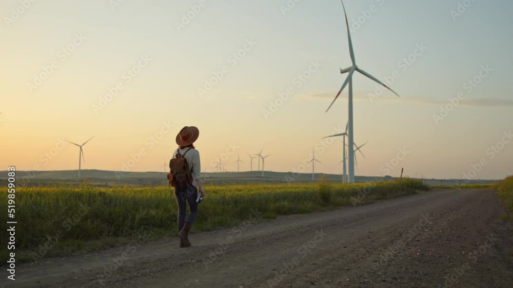 Attractive hiker with a camera walking near a farm with alternative green energy windmills at sunset Attractive hiker with a camera walking near a farm with alternative green energy windmills at sunset