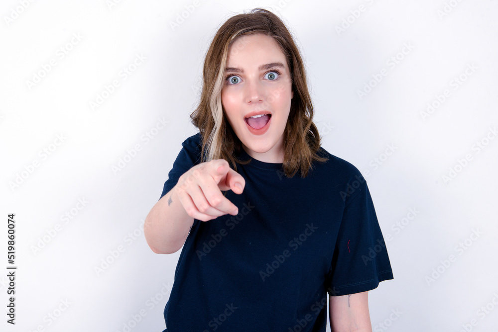Excited positive young caucasian woman wearing black T-shirt over white background points index finger directly at you, sees something very funny. Wow, amazing Excited positive young caucasian woman wearing black T-shirt over white background points index finger directly at you, sees something very funny. Wow, amazing