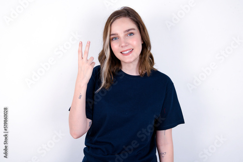young caucasian woman wearing black T-shirt over white background smiling and looking friendly, showing number two or second with hand forward, counting down © Roquillo